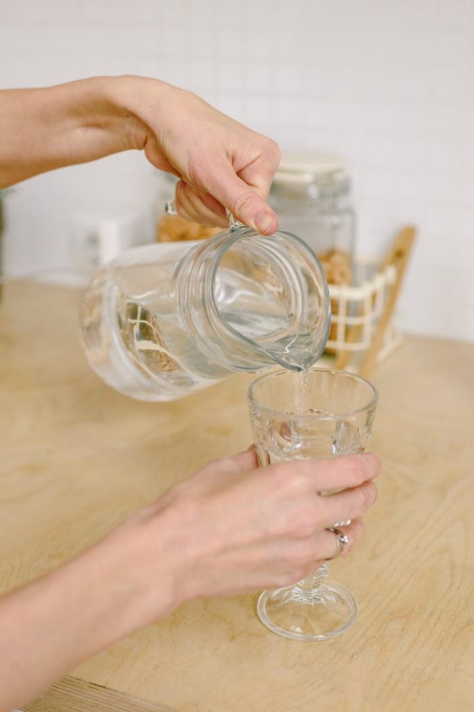 A close-up view of hands pouring water from a pitcher into a glass indoors.